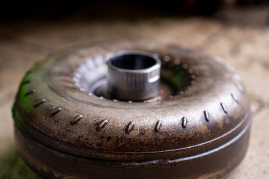 Top view of a used torque converter from an automatic transmission placed on a workshop floor, showing metal housing and central hub.