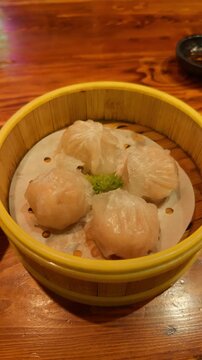 Steaming har gow shrimp dumplings in a bamboo basket, presenting a classic asian dim sum dish on a rustic wooden table evoking traditional chinese cuisine