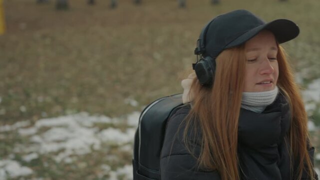 Caucasian redhead girl puppeteering bunny puppet, in snowy park bundled in winter coat and scarf wearing cap and headphones playful interaction shifts to surprised pull as she recoils slightly