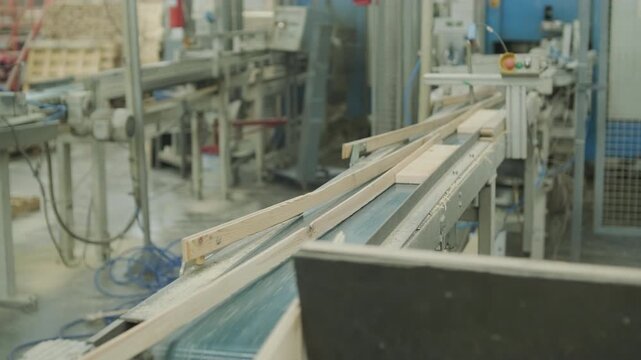 A neat stack of wooden boards on a pallet with a blurred person operating an automated line in the background