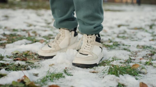 Beige sneakers stepping through melting snow. Lowangle closeups follow furtive figures cautious approach, hesitant pause, quick step suggestive of snatcher, casual green sweatpants, laces scuffing
