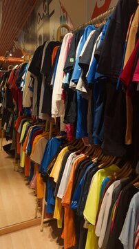 Clothing store interior showing a variety of casual t shirts and other apparel neatly arranged on wooden hangers ready for customers browsing fashion options