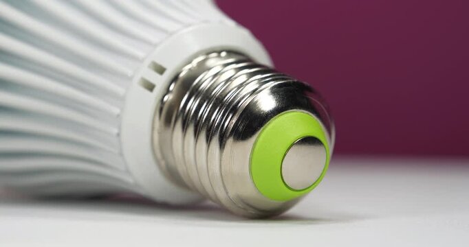 White energy saving LED lamp with E27 screw cap on pink background, close-up