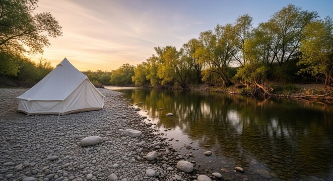 A serene white tent pitched on a rocky riverbank at sunset surrounded by lush green trees on transparent background