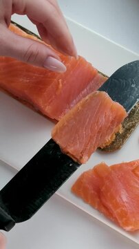 Chef slicing fresh salmon fillet with precision on a cutting board in a professional kitchen. Close-up of hands in black gloves and raw fish texture. High quality 4k footage
