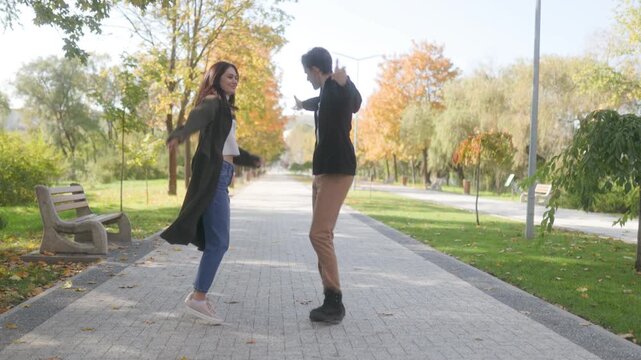 Happy young couple dancing together on paved park path in autumn