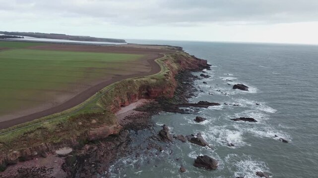 arbroath cliffs east coast of scotland dramatic epic rugged scenery forward movement drone shot red sandstone cliffs stormy sea waves over rocks