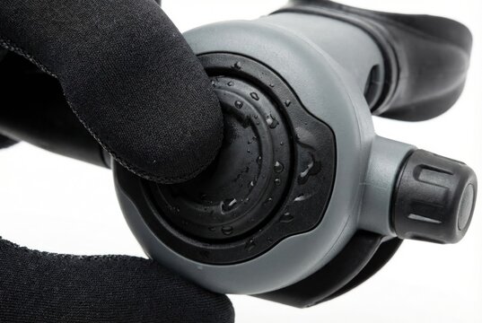 Close up of a diver in black neoprene gloves pressing the purge button on a scuba regulator
