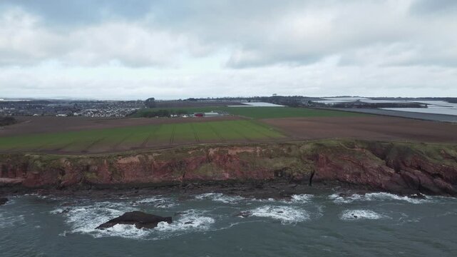 arbroath cliffs east coast of scotland dramatic epic rugged scenery panoramic moving drone shot red sandstone cliffs stormy sea waves over rocks