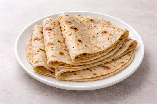 Freshly made roti chapati folded and stacked on a white plate, showing soft texture and light golden spots..A staple South Asian flatbread, perfect for everyday meals and traditional cuisine.