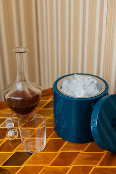 decanter of whiskey, empty glass, and blue ice bucket on midcentury bar cart with wallpaper in background