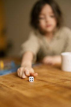 Child plays dice game at wooden table showing focus and fun in simple home moment