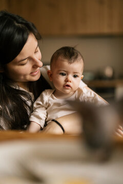 Mother holds baby close in warm kitchen light sharing quiet loving moment together