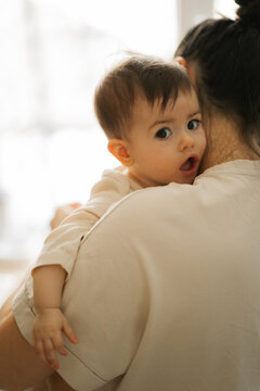 Young child held close by parent in soft natural light showing surprise and wonder during quiet home moment