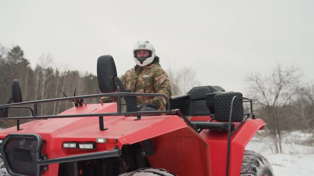 Red atv snowy field rider in camo navigates offroad trail, rear tires kicking snow, overcast sky, pine forest backdrop outdoorsman on winter expedition, throttle bursts and dynamic drift emphasize