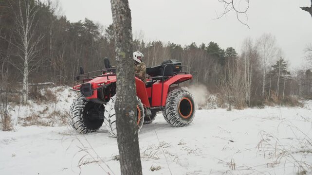 Close red atv parked in snow, oversized studded tires and deep tread dominate foreground, engine and chassis details visible, tree line and frozen field backdrop, quiet anticipation before highenergy