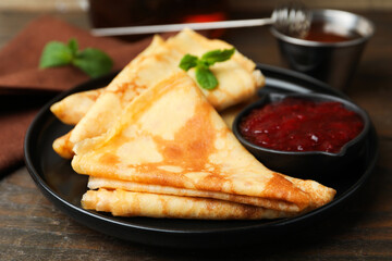 Tasty crepes with mint leaves and jam served on wooden table, closeup © New Africa