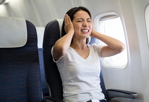 Woman suffering from ear pain due to pressure change during flight. Passenger experiencing sharp discomfort and barotrauma inside airplane cabin. Travel health and medical issue concept.