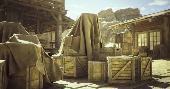 A rustic western town features covered crates and wooden buildings under a clear sky. Dusty landscape and mountainous backdrop enhance the old frontier atmosphere during daylight.