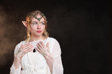 Obraz premium Beautiful girl dressed as elf on black background with smoke, space for text