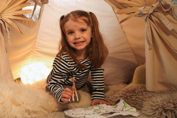 Little girl with drawing of map and toy giraffe near wigwam at home © New Africa