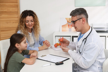 Obraz premium Endocrinologist in glasses consulting woman with her daughter and showing model of thyroid gland at white desk in clinic