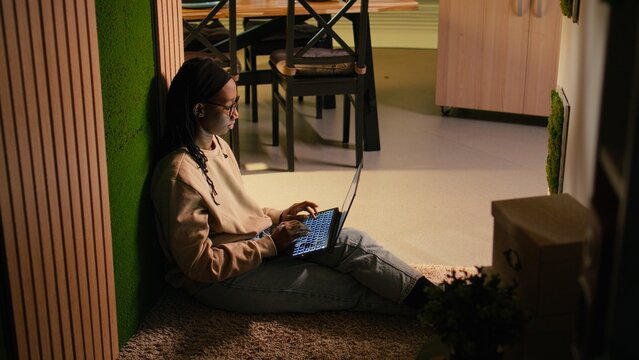 Young black woman with laptop sitting in the hallway in cozy warm interior, natural peace calm moment browsing websites and enjoying time at home. Cozy lifestyle and relaxing screen time habits.