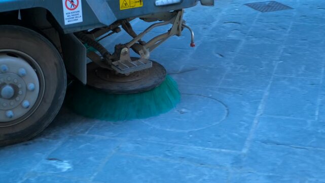 Street sweeper vehicle cleaning city pavement. Close-up of a municipal sweeper machine with a rotating brush cleaning a cobblestone city street, highlighting the urban sanitation