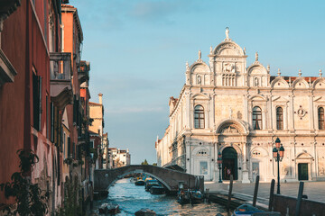 Magnificent facade of the Scuola Grande di San Marco by a Venetian canal. Renaissance architecture, stone bridge, and boats in Venice, Italy, during golden hour. © Maria Sap