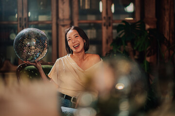 Naklejka premium Happy young asian woman smiling and laughing, holding disco ball, celebrating an event at a party or nightlife venue