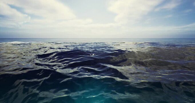 Gentle waves roll across the serene ocean surface as the sun sets, creating a tranquil atmosphere with soft clouds scattered across the expansive blue sky.