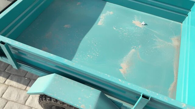 Top view empty trailer bed showing green metal frame and worn plywood floor with edge chips and small damage, sunlight casting.