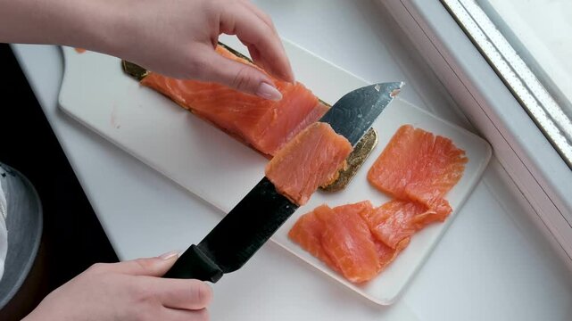 Chef slicing fresh salmon fillet with precision on a cutting board in a professional kitchen. Close-up of hands in black gloves and raw fish texture. High quality 4k footage
