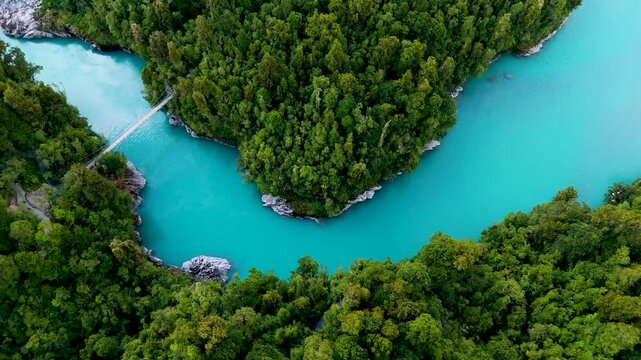Aerial view of the Hokitika Gorge where turquoise waters meander through lush green forests, with a suspension bridge spanning the divide, Kokatahi, New Zealand.