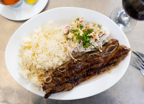 Latin american dish Churasko - barbecue ribs, complemented by boiled rice and vegetable salad. Bowl with red spicy sauce served with dish..