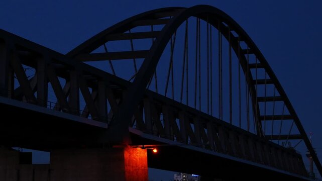 Steel arch bridge at blue hour with train lights and urban skyline, night architecture and transportation scene