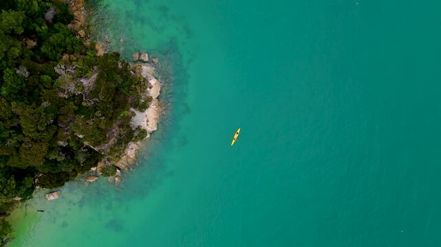 Aerial view of kayak in turquoise water next to a lush coastline, contrasting the vibrant sea and the wild vegetation, Abel Tasman, Tasman Region, New Zealand.