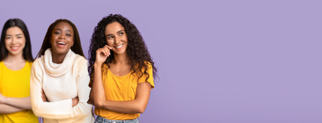 Fototapeta premium A brunette woman looks thoughtfully to the side while smiling. She stands against a purple background. Her pose suggests she is considering a great idea or opportunity.
