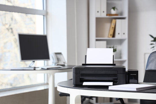 Modern printer with paper sheets on desk in office