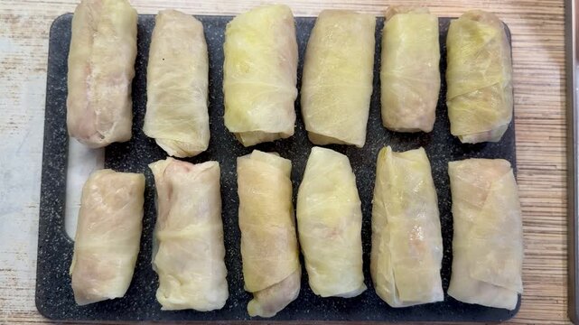 Cabbage rolls on black cutting board closeup, uncooked meat filled cabbage leaves rolled into neat cylinders, arranged in rows.