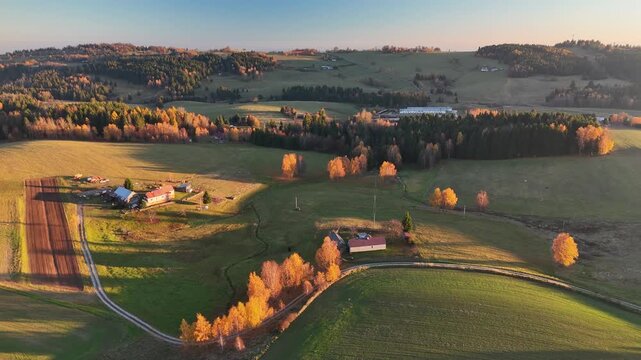Aerial view of golden sunlight illuminating a landscape of farmland, forests and buildings, creating a tapestry of color, Detvianska Huta, Banska Bystrica Region, Slovakia.