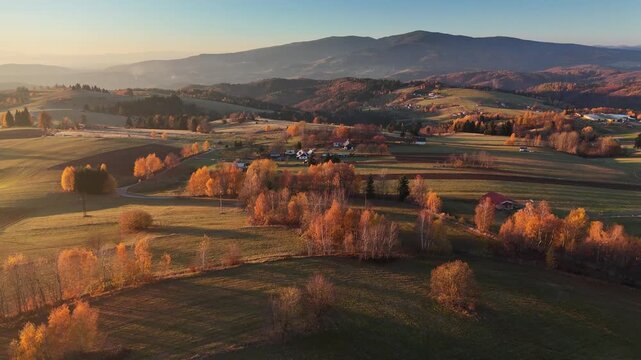 Aerial view of fields and scattered houses amidst the rolling hills during golden hour, creating a patchwork of textures and tones, Detvianska Huta, Banska Bystrica Region, Slovakia.