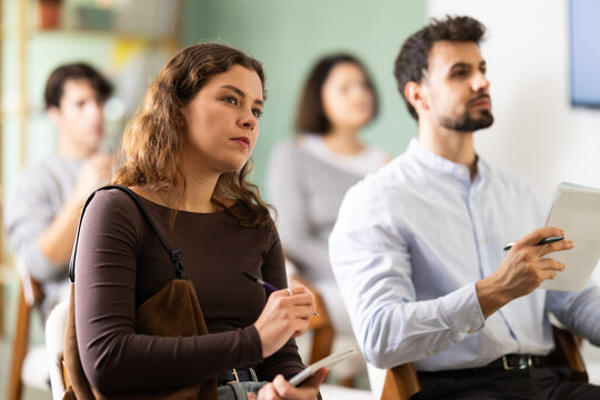 Woman listens attentively to teacher and takes notes in notebook during a professional development course