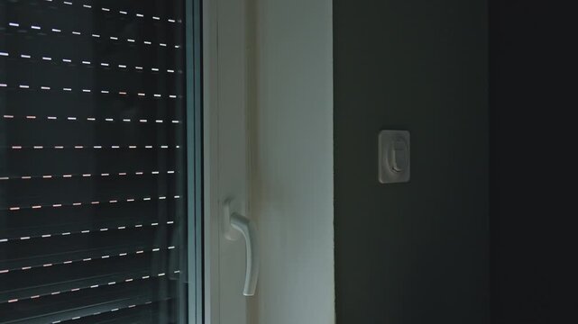 Woman presses wall switch as exterior roller shutter rises on window