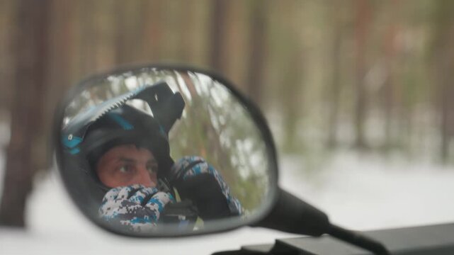 Helmeted rider reflected in mirror, visor and patterned glove visible, snowy pine forest backdrop, closeup contemplative expression, rider scanning trail ready for extreme offroad adventure