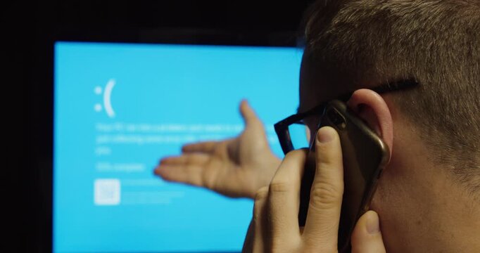 Man calling support after computer problem with blue screen, representing technical issue and troubleshooting.
