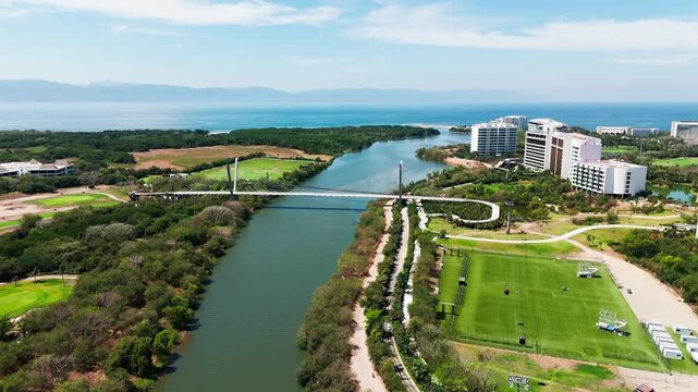 Aerial view of a bridge over the river, with golf courses, buildings, and lush green spaces, creating a vibrant contrast, Nuevo Nayarit, Nayarit, Mexico.