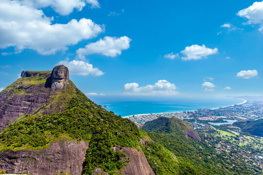 Breathtaking aerial view of Pedra da G&aacute;vea mountain overlooking Barra da Tijuca beach and the Atlantic Ocean in Rio de Janeiro, Brazil. A stunning landscape featuring lush green peaks and city.
