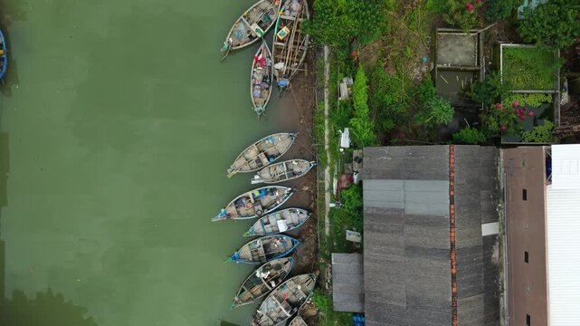 Aerial view of boats docked along the riverbank next to the Jepara Floating Fish Market, contrasting with the adjacent buildings, Jepara, Central Java, Indonesia.
