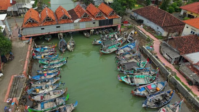 Aerial view of boats lining the waterway next to the Jepara Floating Fish Market, contrasted with the red-tiled roofs of surrounding buildings, Jepara, Central Java, Indonesia.